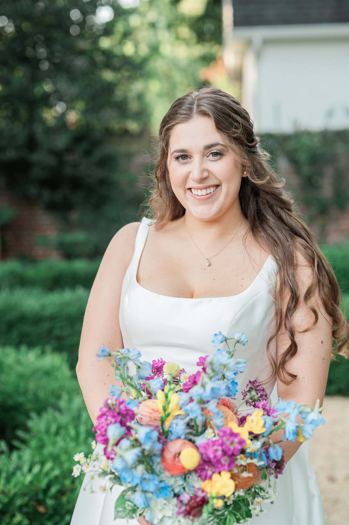 A bride smiling while holding a colorful bouquet of flowers