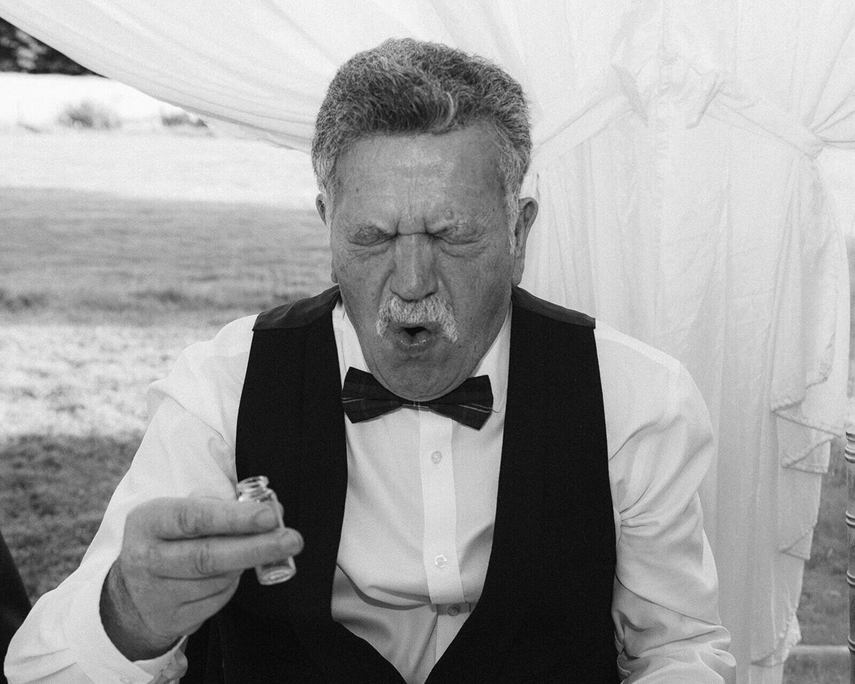 A man drinks a shot at a wedding and his face is shocked by the strong alcohol