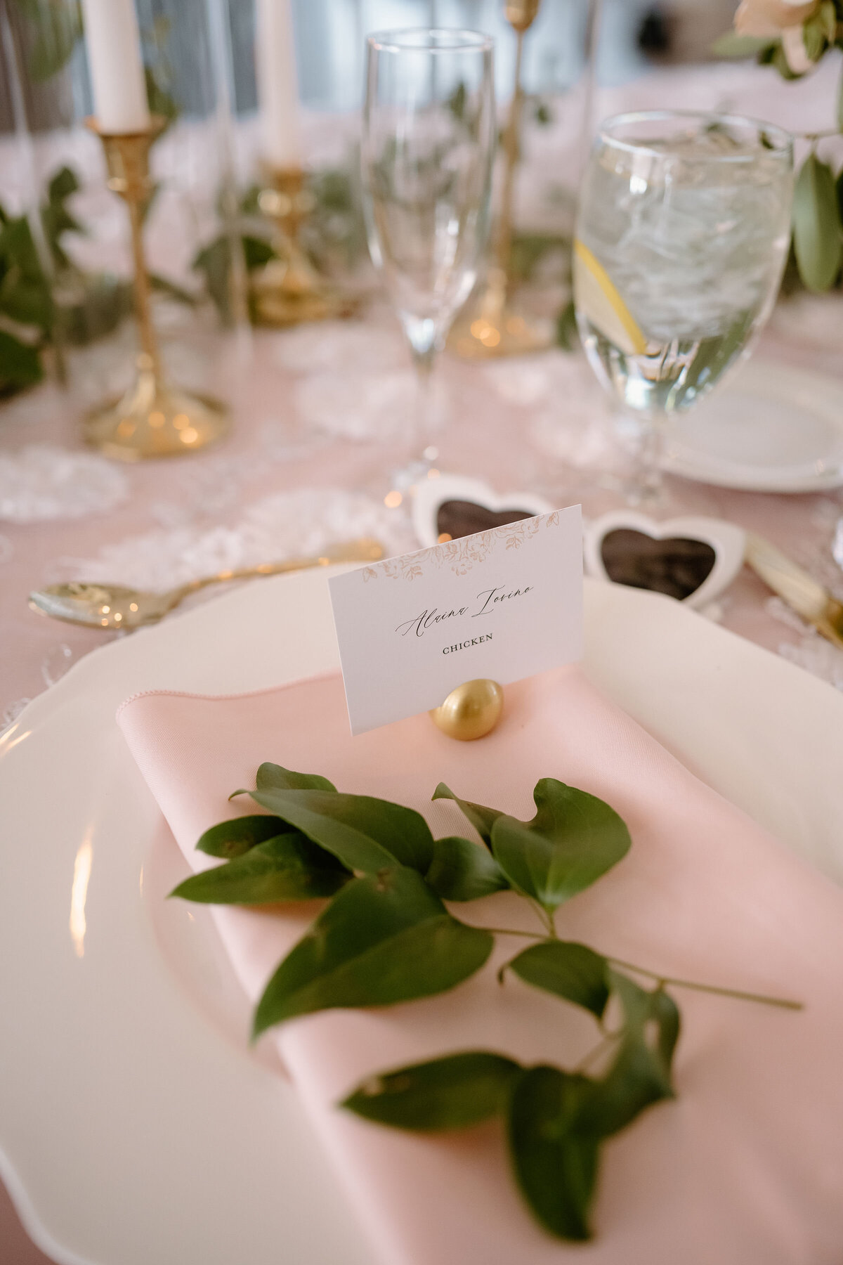 Elegant place setting with pink napkin, greenery, gold name card holder, and heart favor.