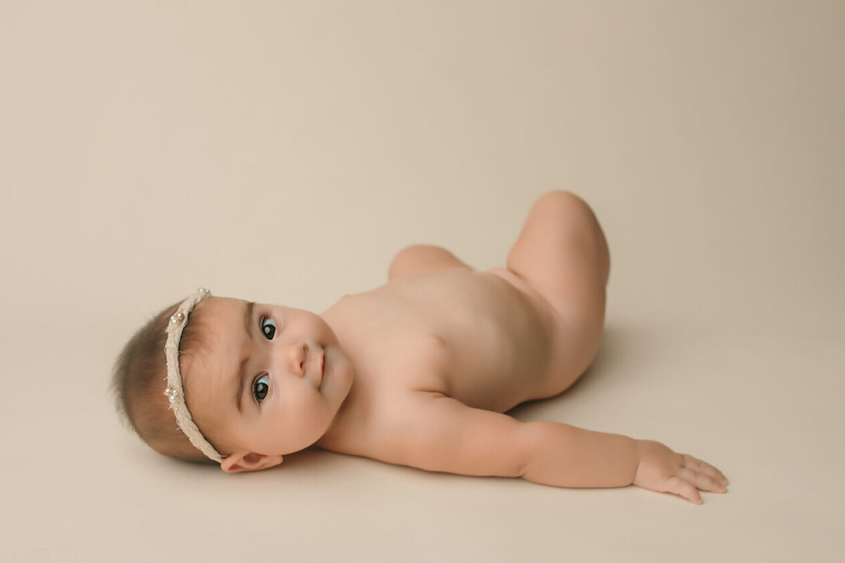 a six month old girl laying on her back nude looking at the camera