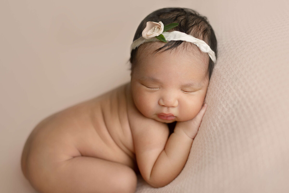 baby girl laying  on her tummy on a  pink  backdrop in  newborn session