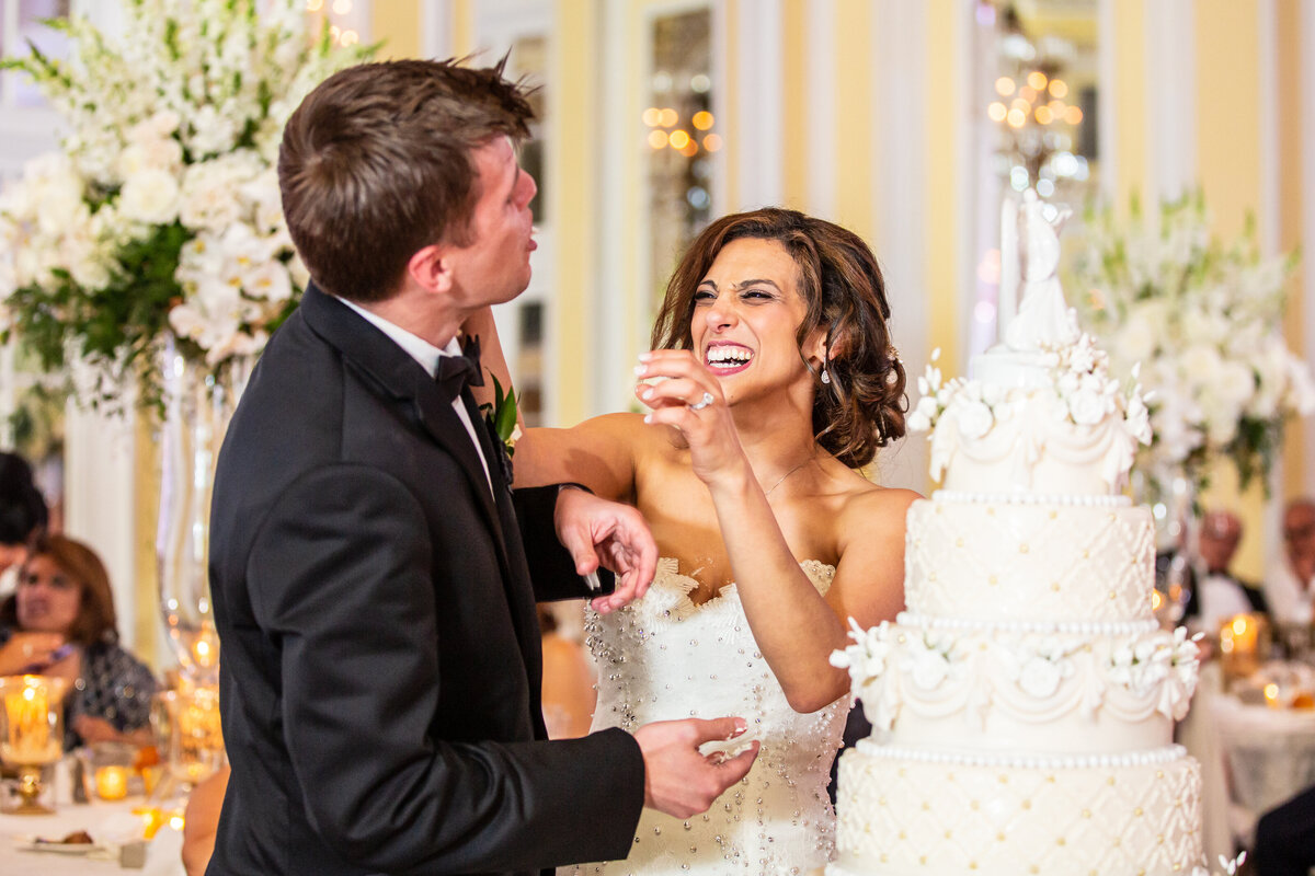 A bride and groom smash cake in each others faces at their wedding.