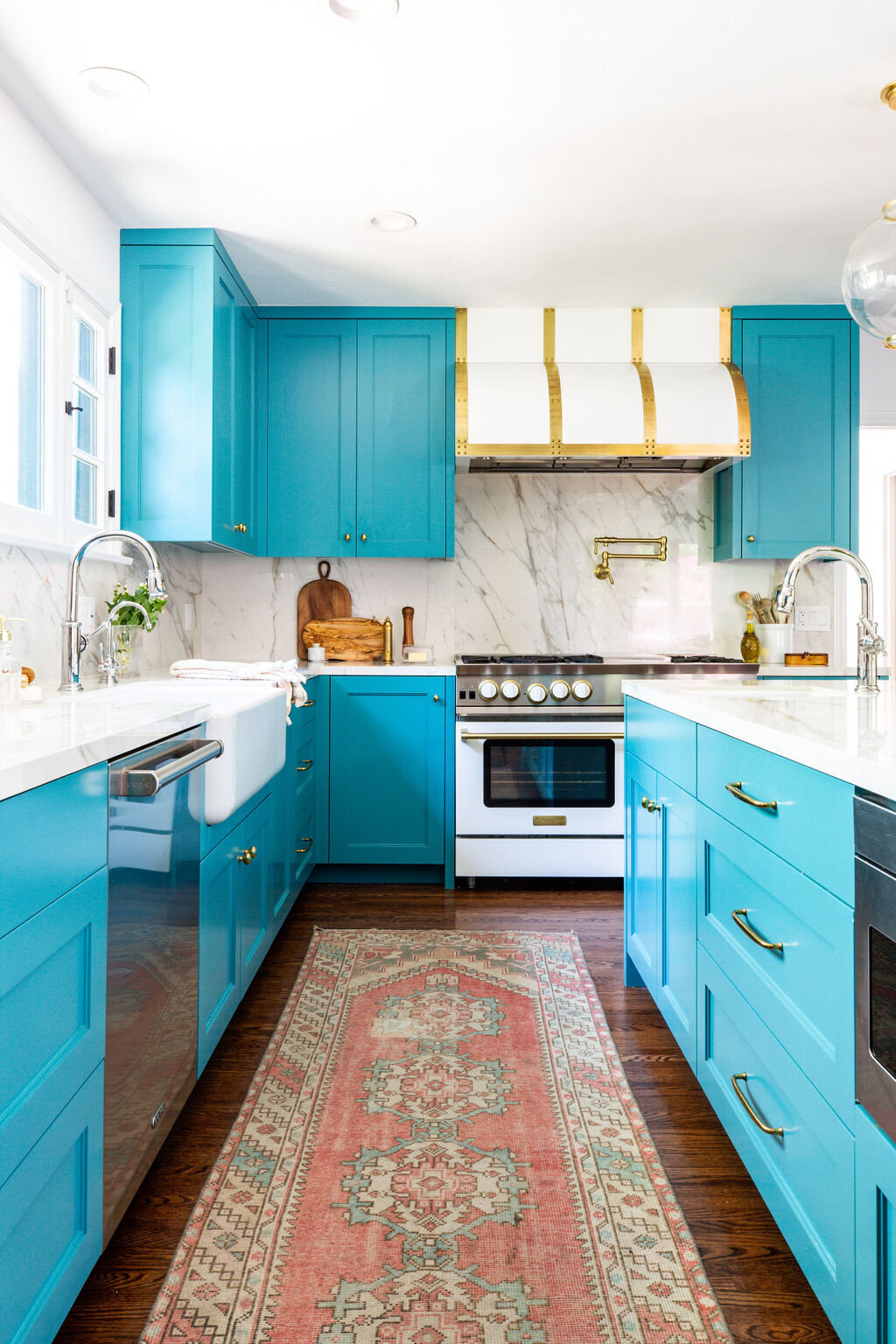 Kitchen with Teal cabinets, marble backsplash, and white and brass Blu Star range and hood.