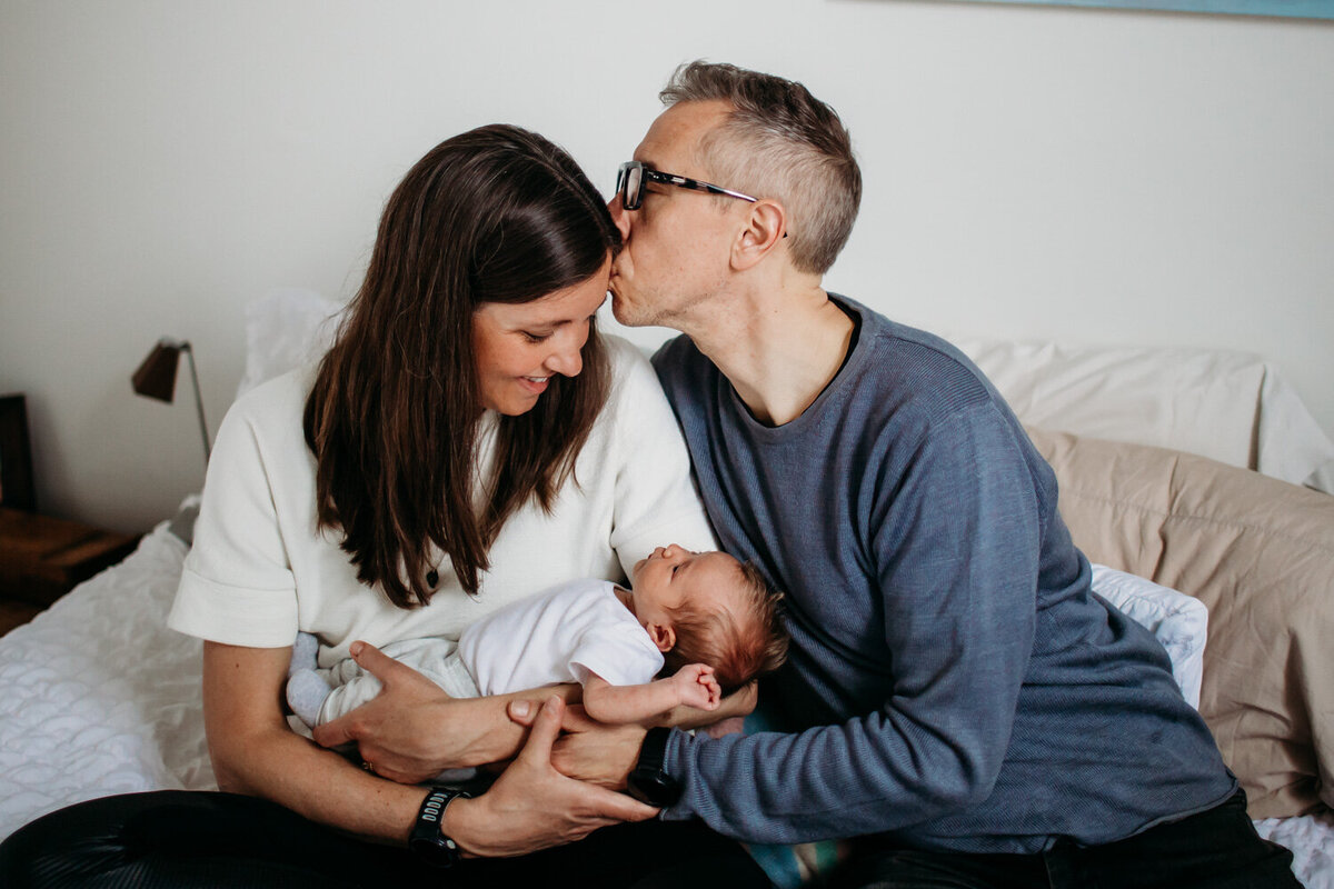 Husband giving wife gentle kiss while she holds their new daughter