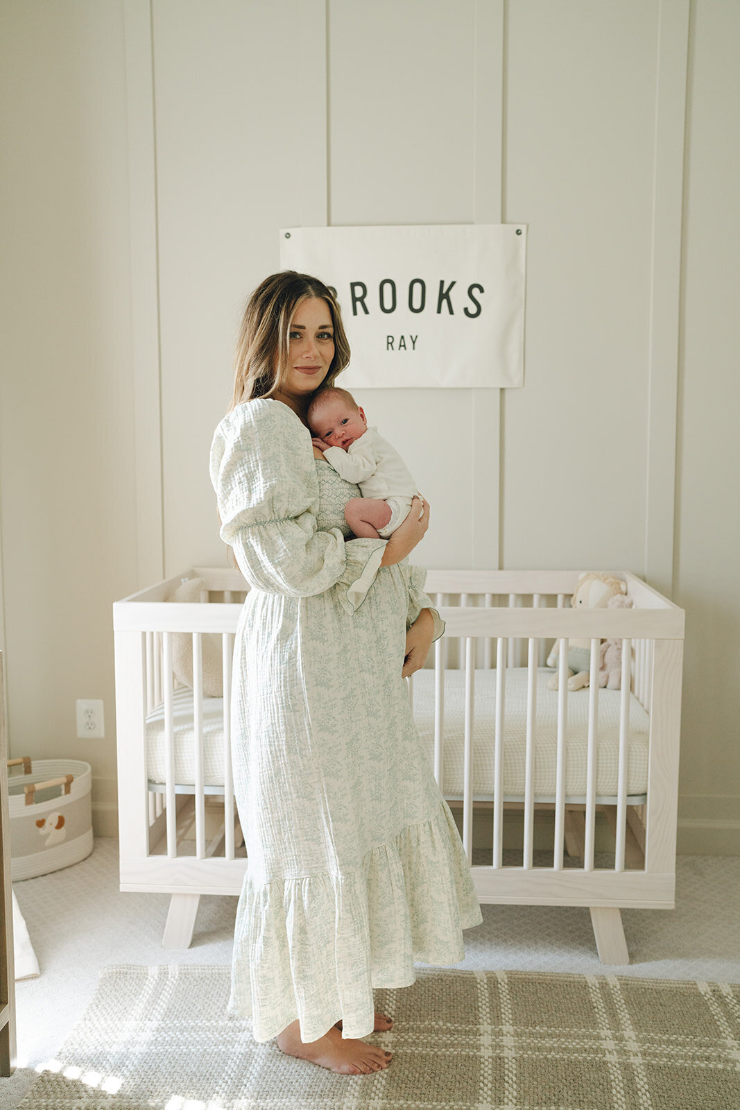 Mom holding her baby in the nursery and looking at the camera during a quiet in-home photo session