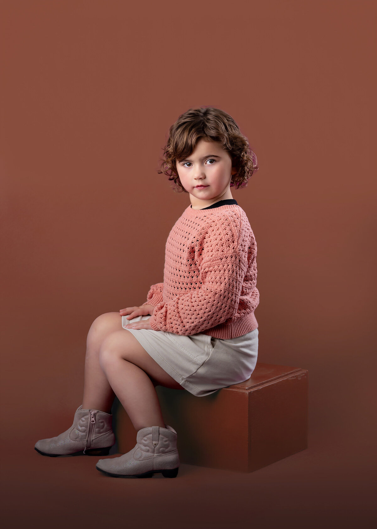 Girl sits looking serious on an orange box on a orange background