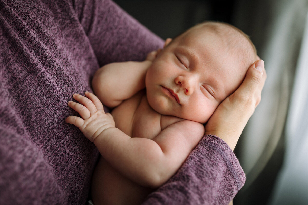 newborn in just diaper asleep in mom's arms at home