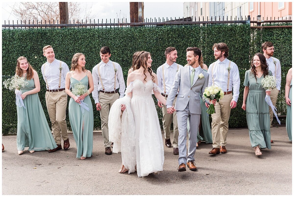 Bride and groom walk hand in hand with their wedding party walking close behind them for a fun candid wedding party shot captured by Denver wedding photographer at skylight venue