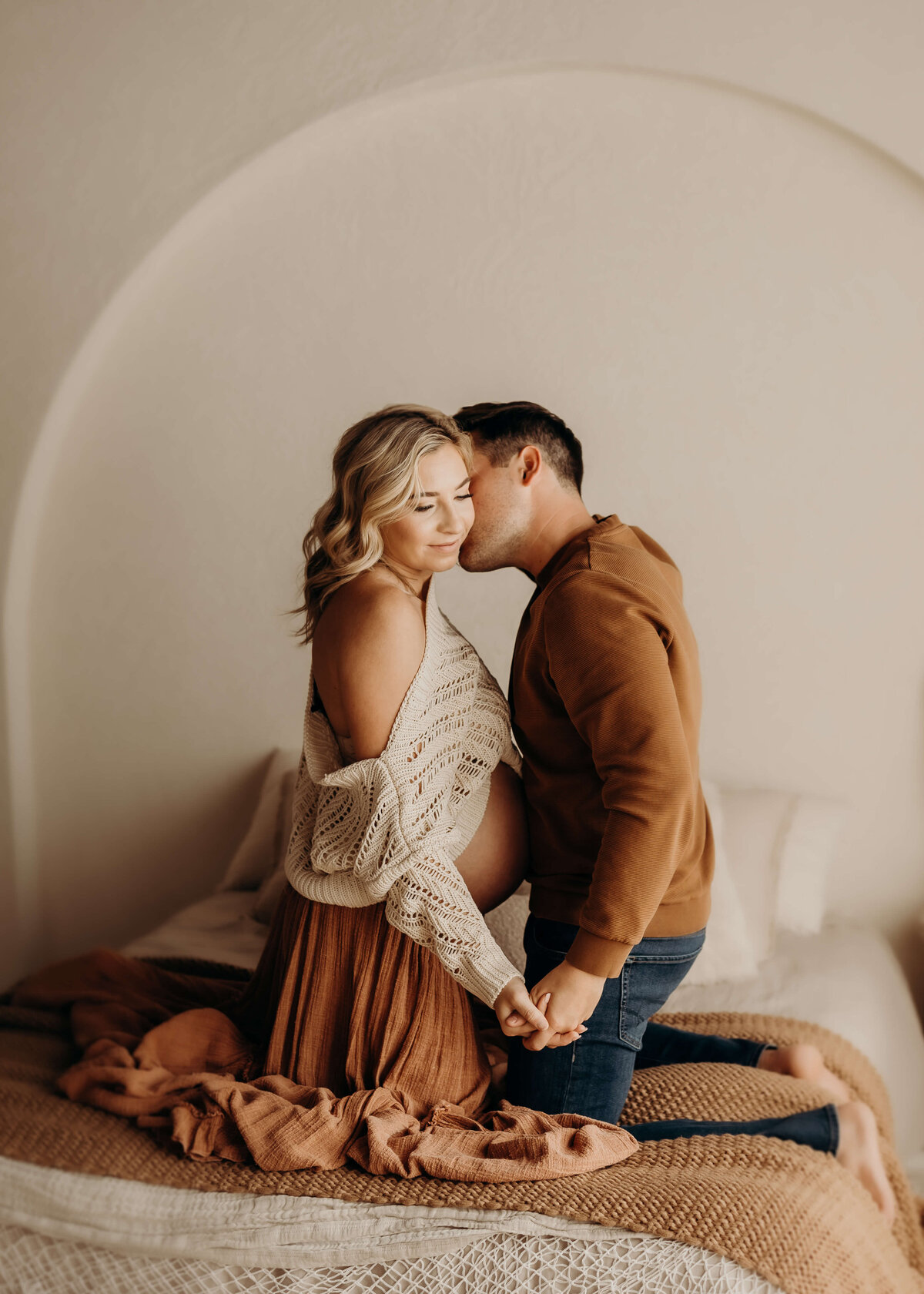 husband faces pregnant wife on bed kissing her cheek