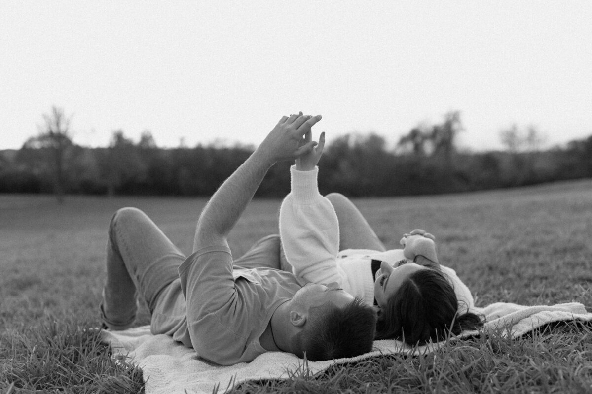 A couple laying on a blanket in an open field