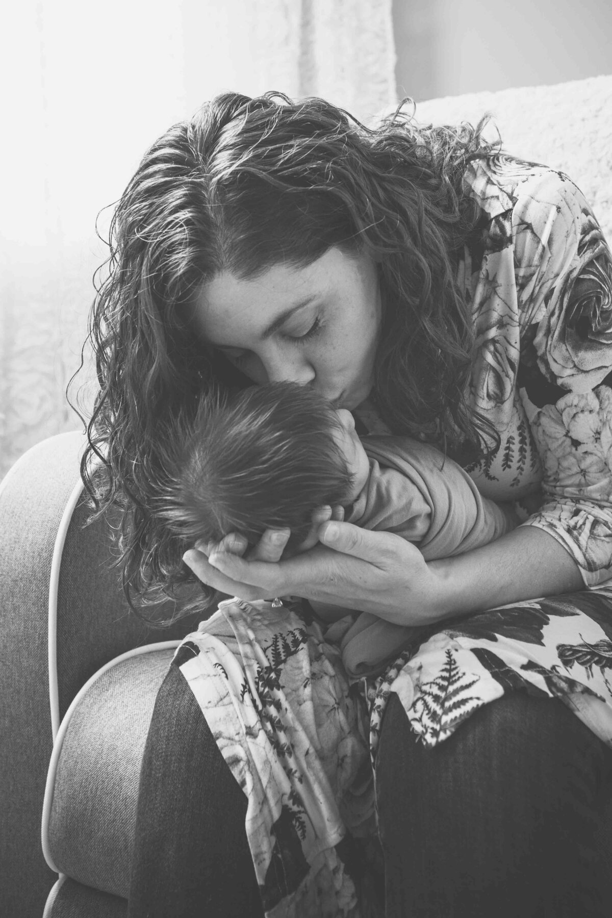 a black and white photo of a mother kissing her baby for their newborn photography