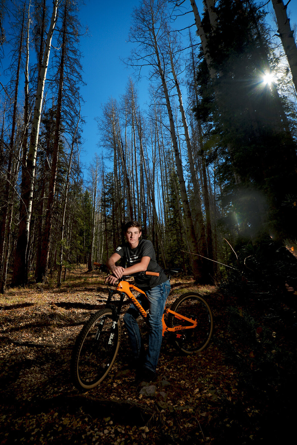A mountain biker leans on his orange bike in a forest trail