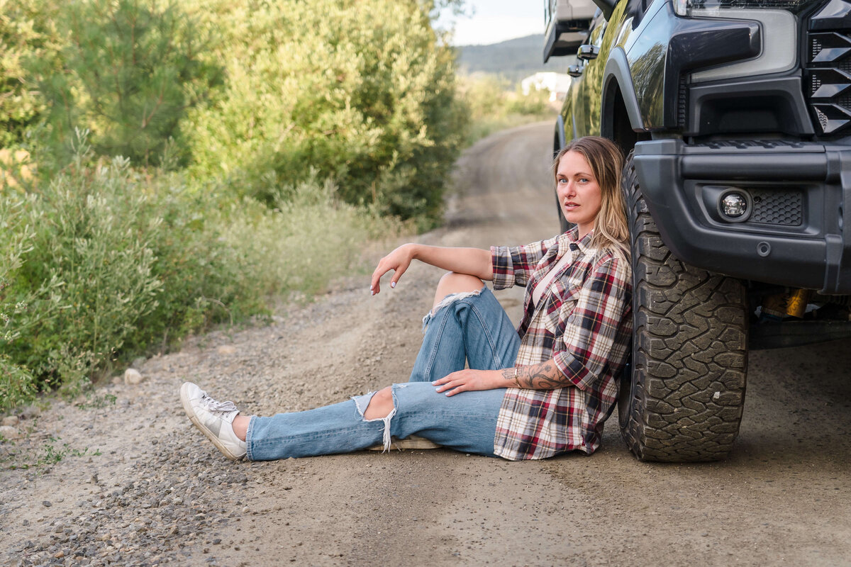 relaxed woman sitting against black truck on a deserted country road for adventurous brand shoot
