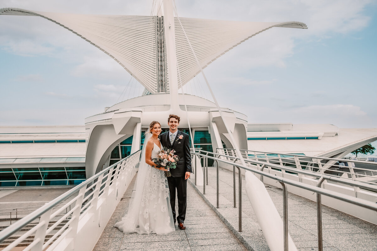A bride and groom stand together smiling on the Milwaukee Art Museum skyway walking path