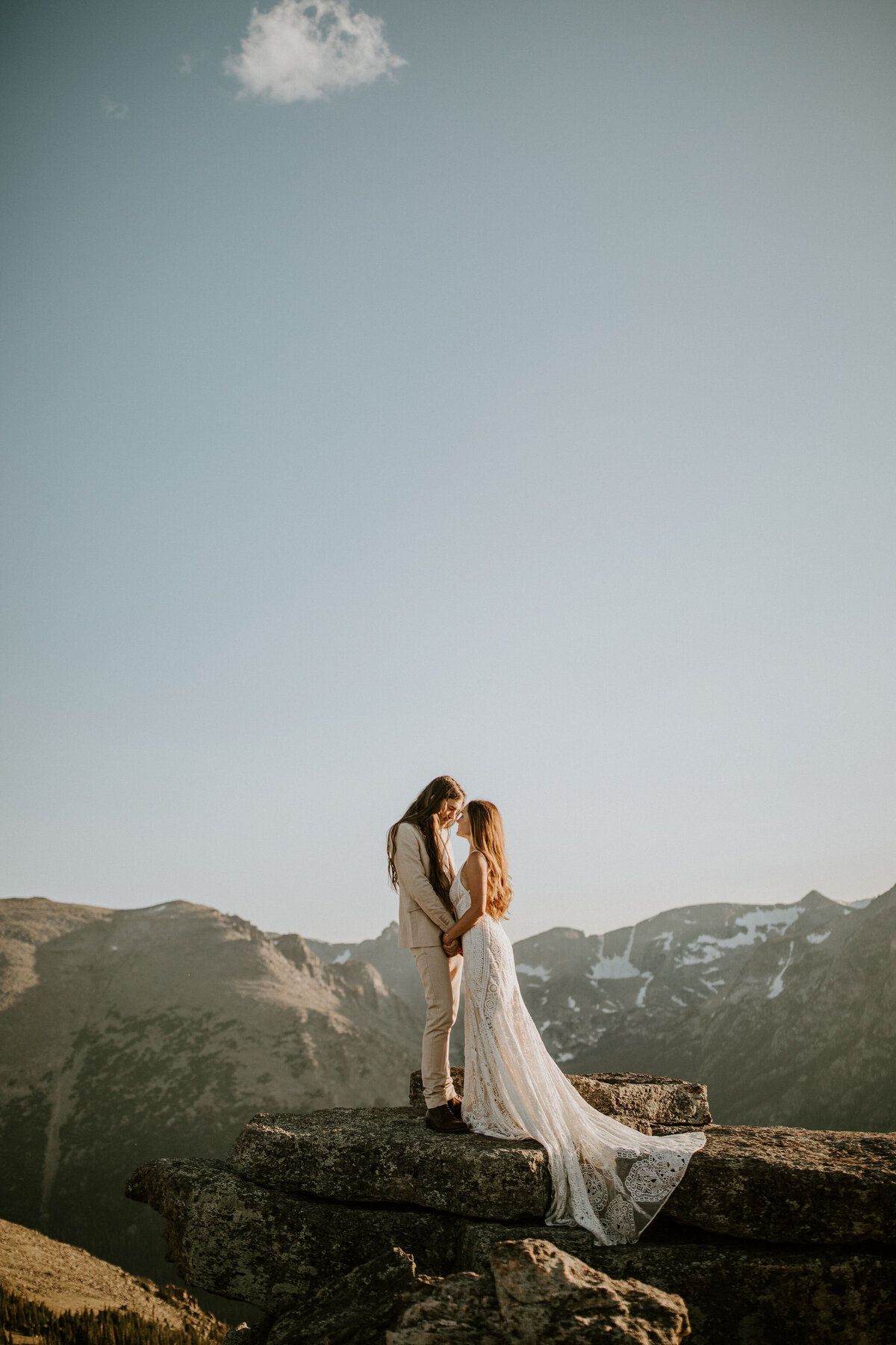 Bride and groom wearing an ivory suit and white wedding gown atop a mountain stone with the landscape in the back.