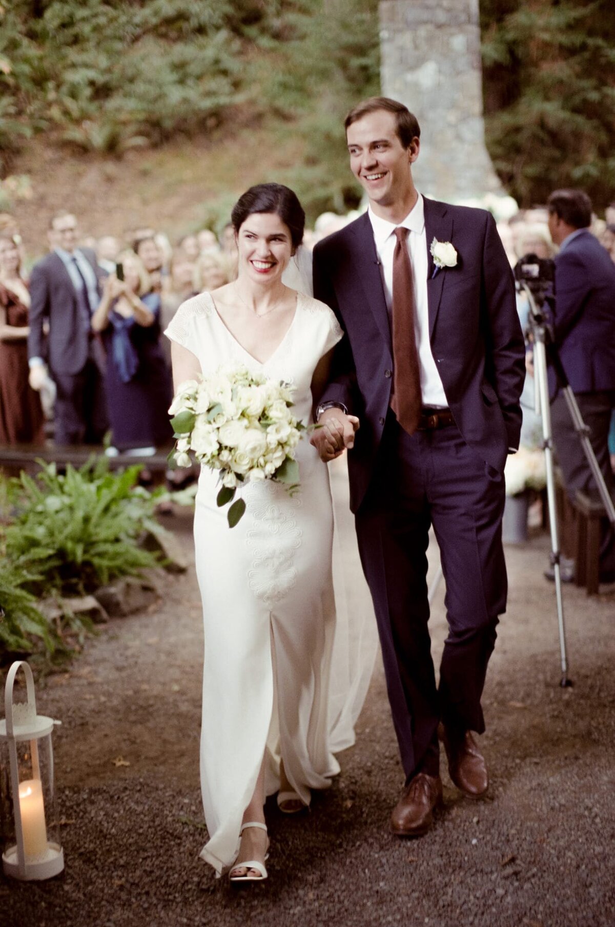 Newly married man and his wife walk back up the aisle in a picturesque forest wedding while entertaining applauses from their guests.