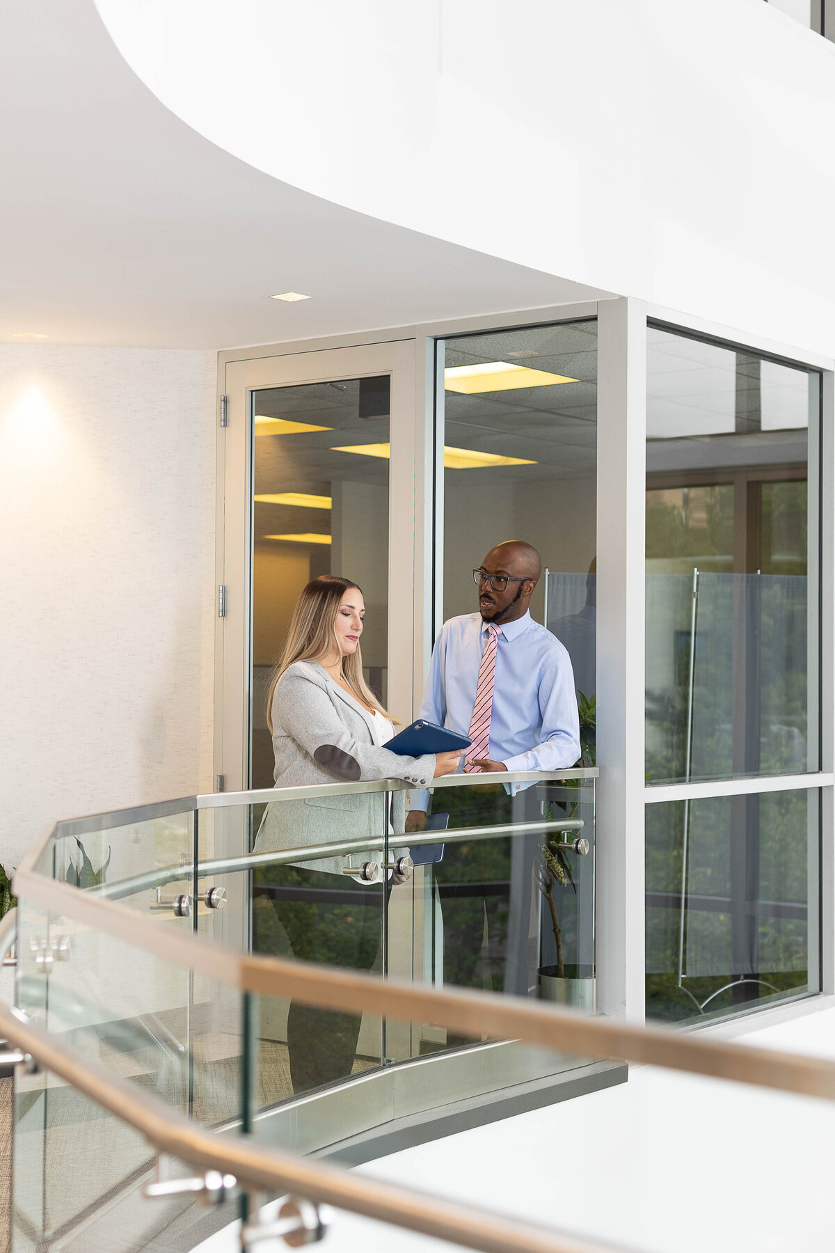 caucasian businesswoman showing african-american male businessperson a folder in a glass hallway