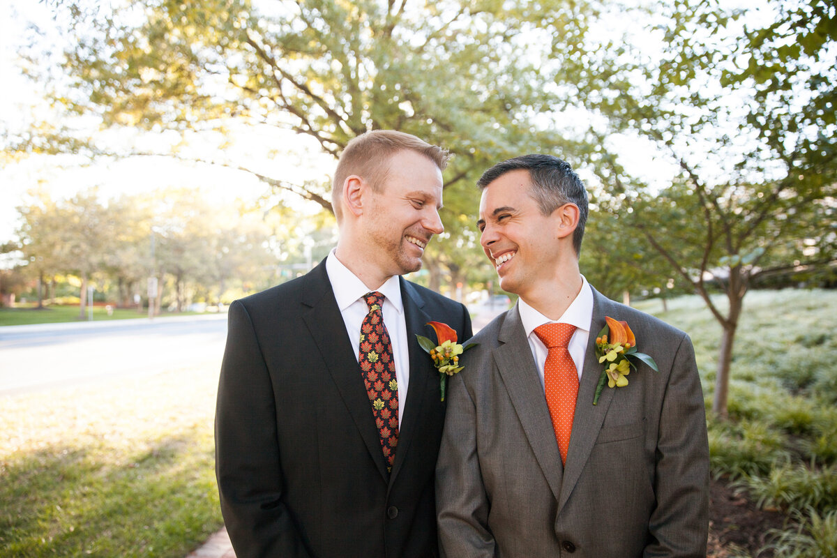 Two grooms standing close together smiling at each other 