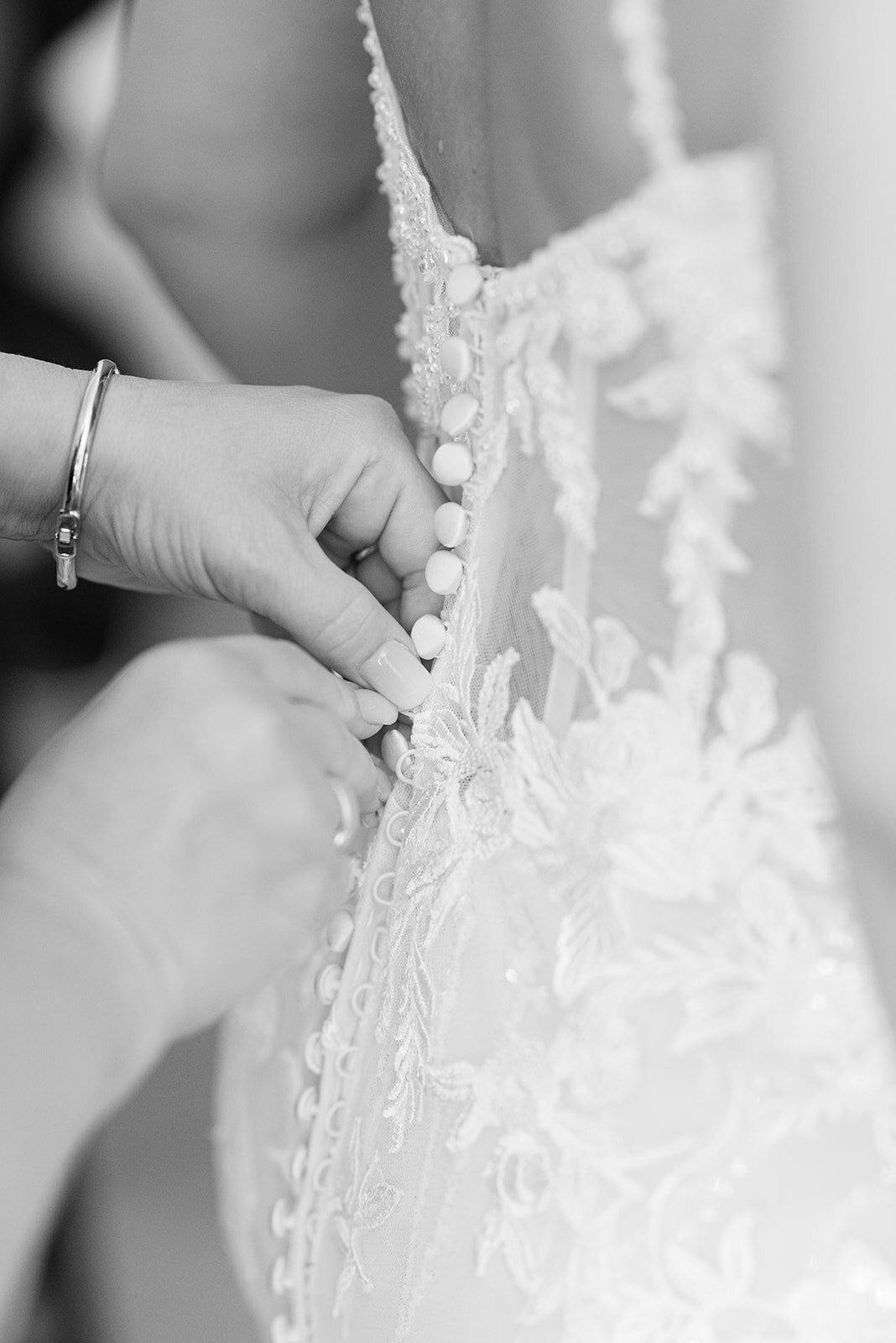 Black and white image of a bride in her dress, details of the dress being done up.