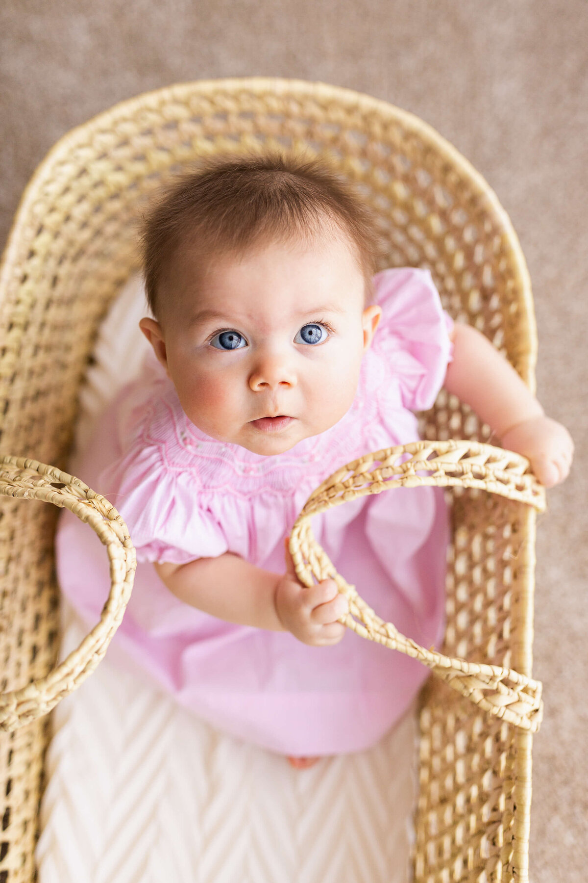 Six month old sits in a Moses basket and looks up