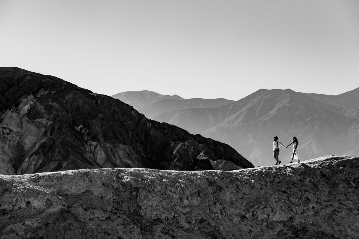 Bride and Groom walk atop a hillside mountain with a breathtaking mountain backdrop in Death Valley National Park California, Photo by Tanya Parada