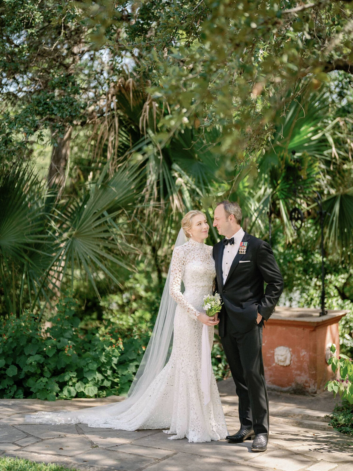 Groom-in-black-tuxedo-looks-at-bride-in-white-dress-and-veil-for-in-garden-at-laguna-gloria-wedding