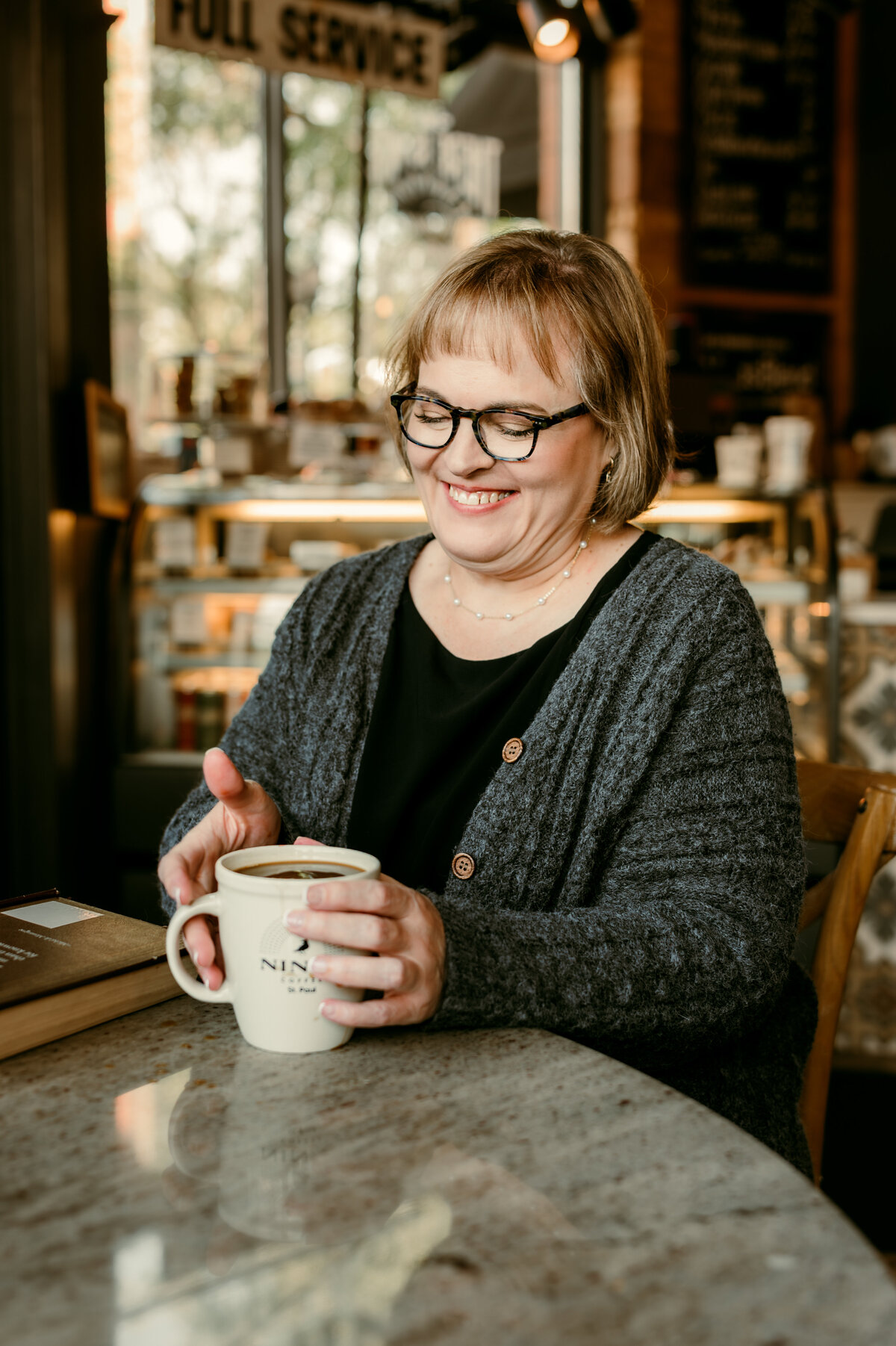 Warm and candid online dating photo of a woman sipping coffee at Nina’s Coffee Shop in St. Paul, captured with natural light for an approachable and authentic vibe