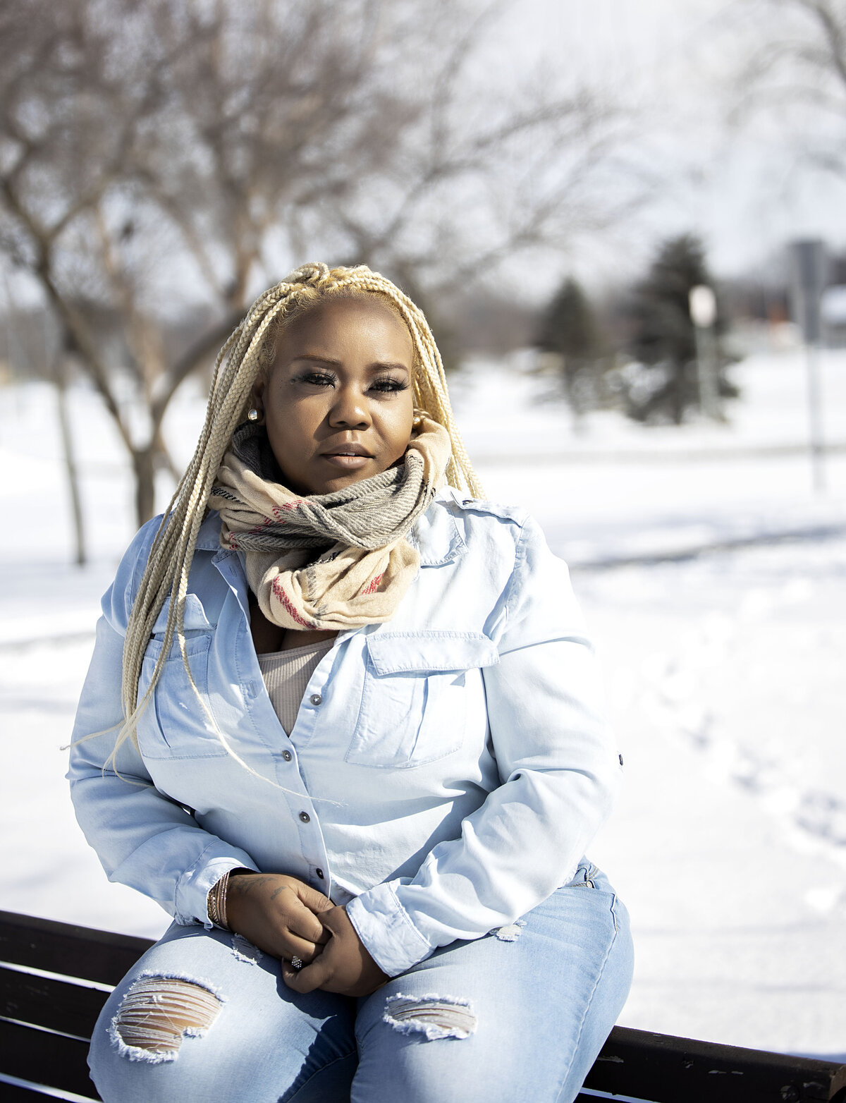 Woman in black leather jacket, blue jean top and jeans sitting on park bench