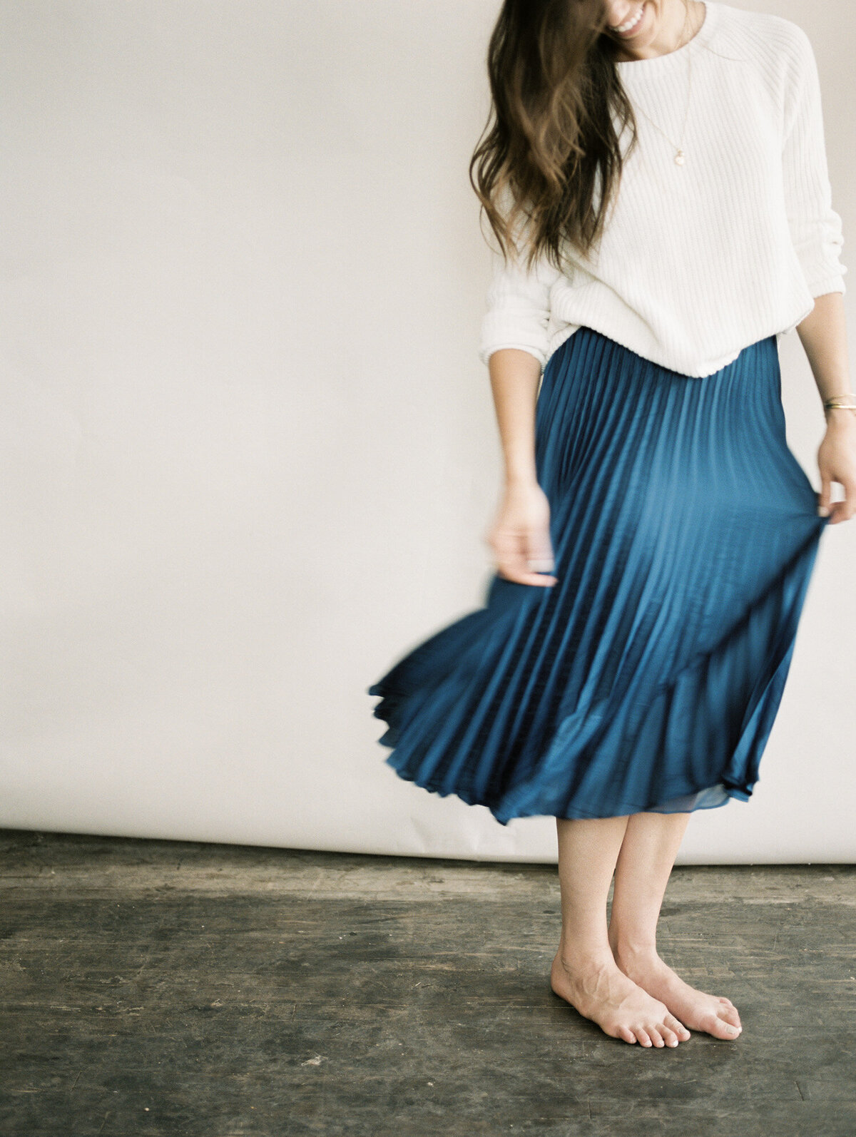woman in cream sweater, royal blue pleated skirt, barefoot 