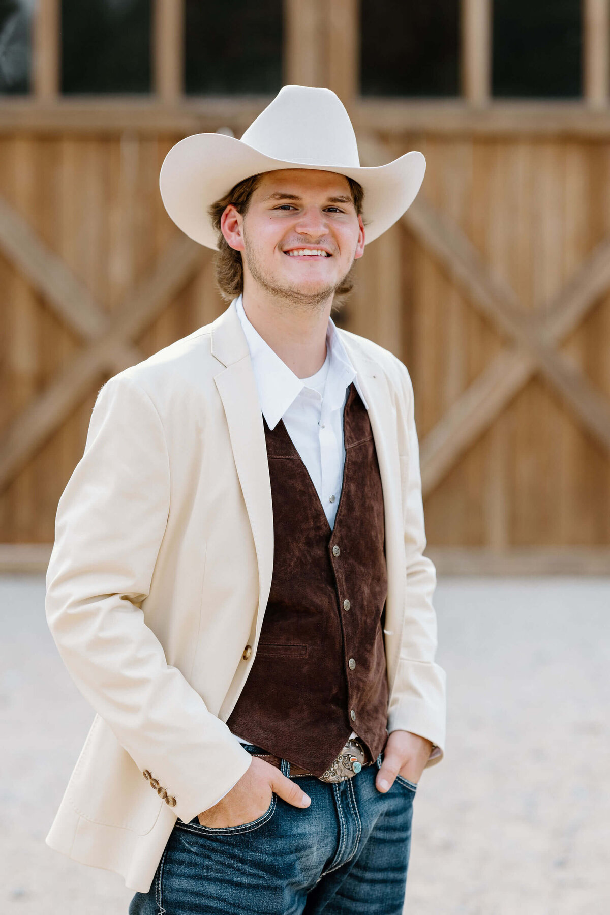 grooom on wedding day  in white coat, cowboy hat, suede vest, and cowboy boots