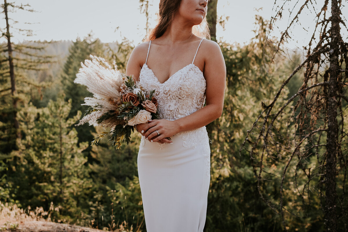 Close shot of brides dress as she stands holding bouquet.