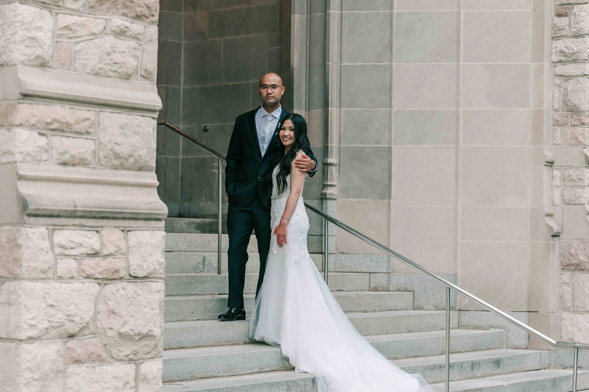 Bride and groom standing next to each other on the university campus stairs.