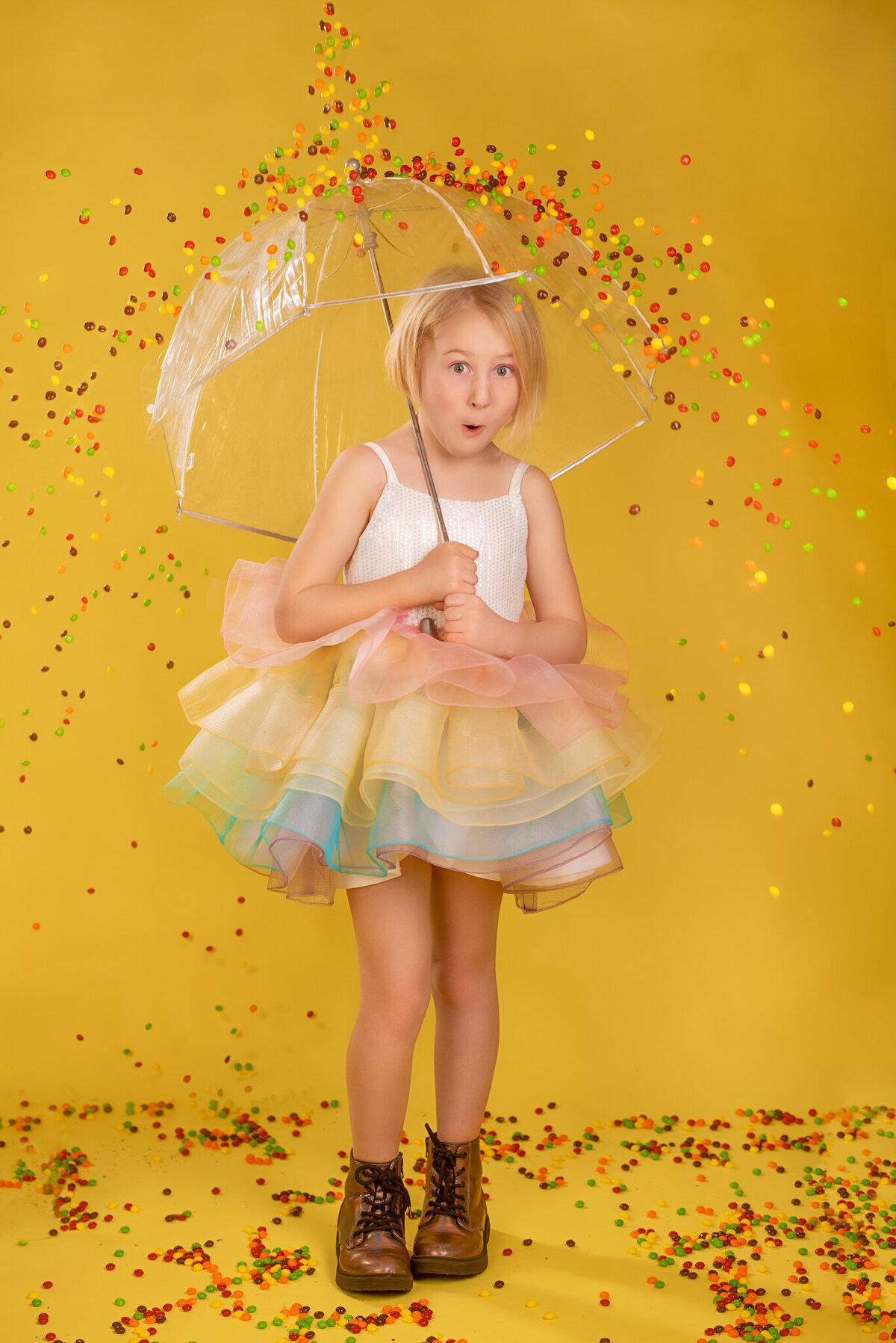 Colorful portrait of a young girl in a rainbow dress, surrounded by falling Skittles in a whimsical and playful scene. Captured in Overland Park, Kansas, this vibrant setup is perfect for families seeking creative and joyful child photography.