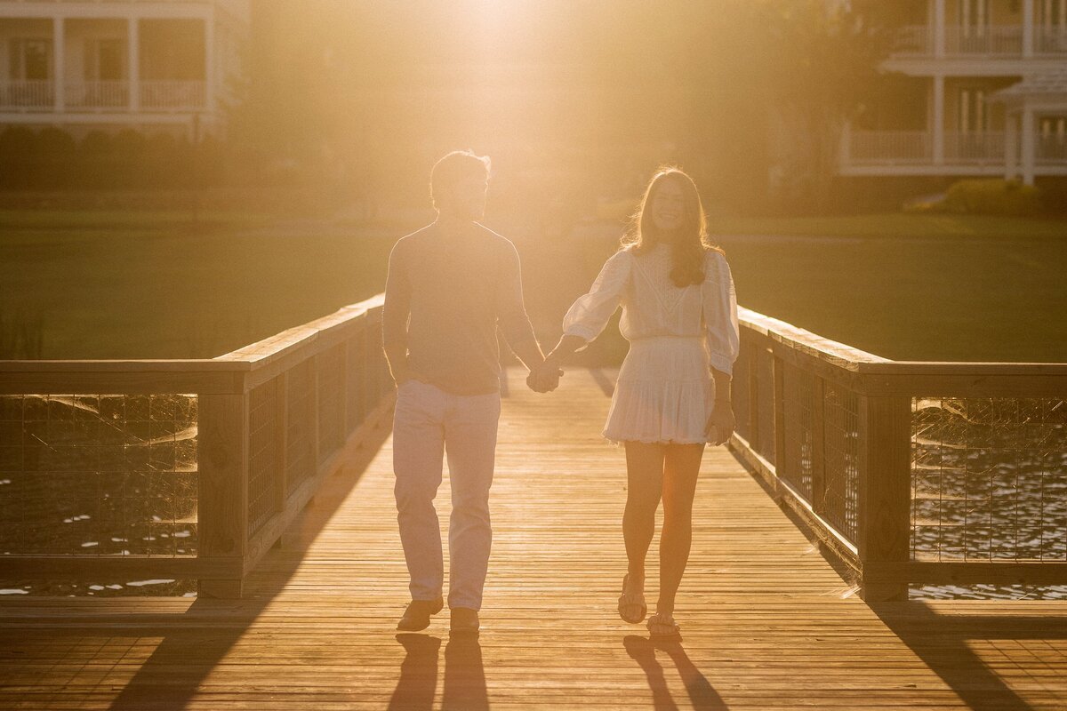 couple walks hand in hand down a dock at sunset