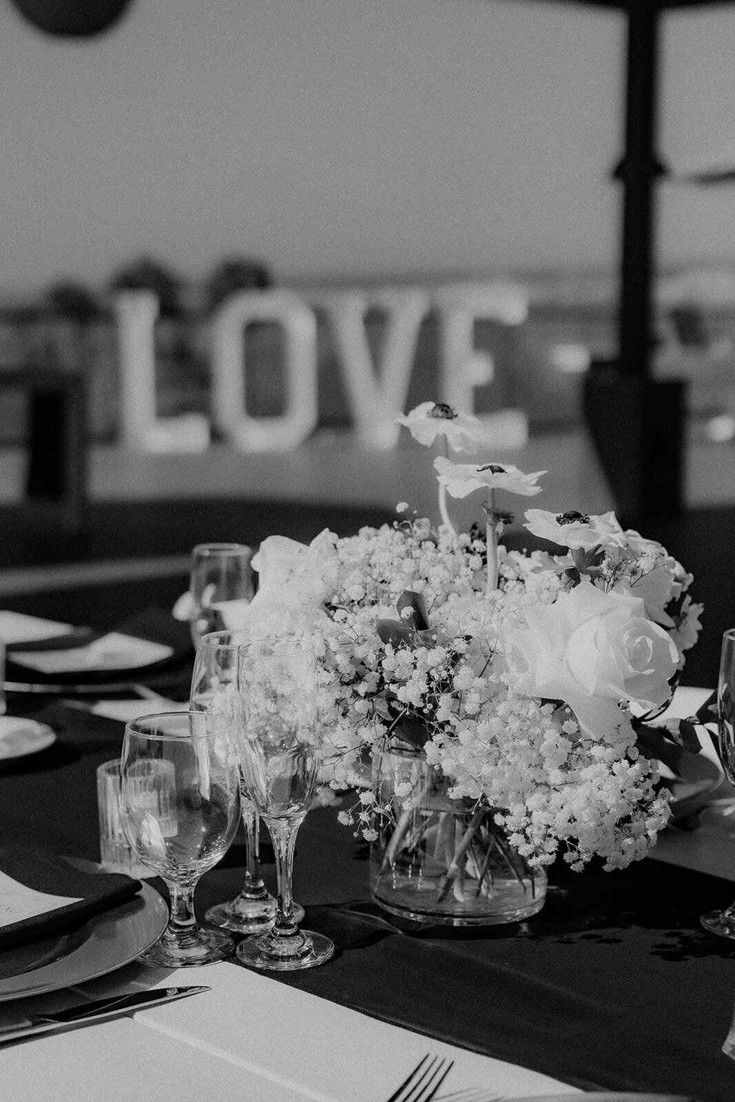 Black and white close up of wedding table and centerpieces with "LOVE" sign in background  at San Diego wedding