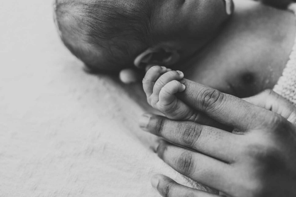 Ruua Hamdan Photography (Altrincham/Manchester, UK): A black and white, close-up image shows a baby's hand gently holding an adult's finger.