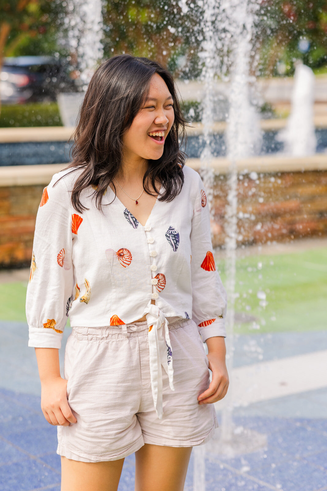 teenager girl laughing off camera with the fountain in the background in Sandy Spring during senior portraits session