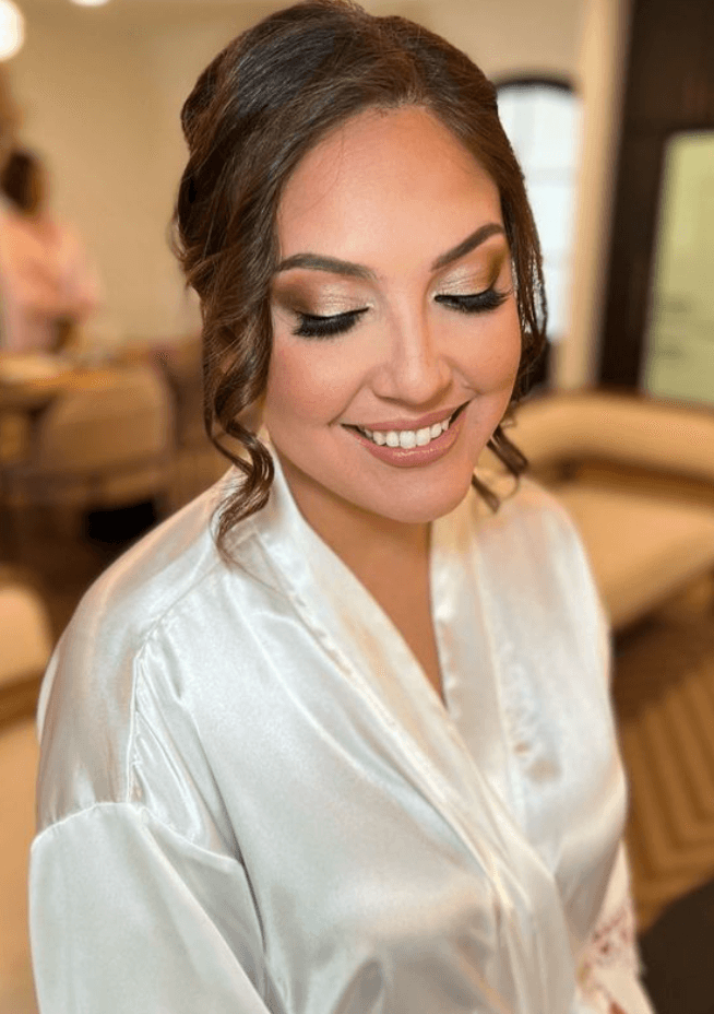 Bride with curled updo and gold eyeshadow smiling softly, styled by professional bridal makeup artist in Austin