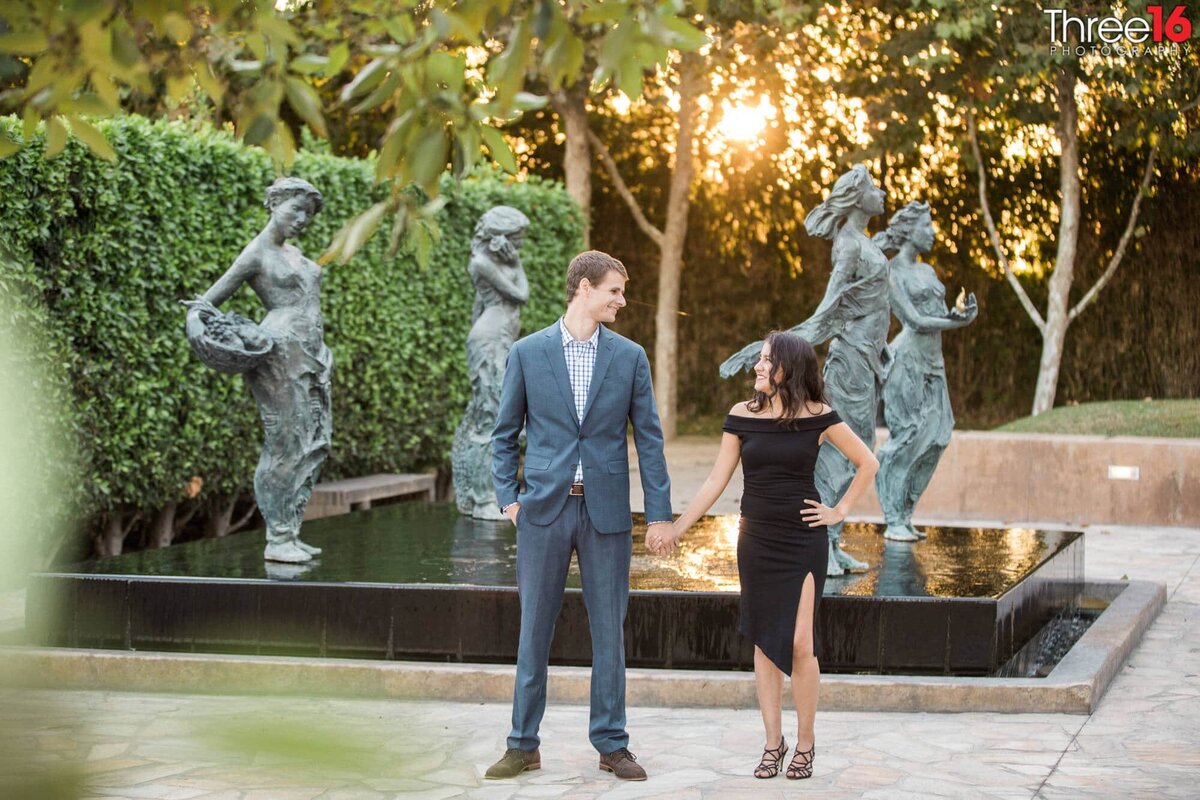 Engaged couple stand in front of art sculptures holding hands