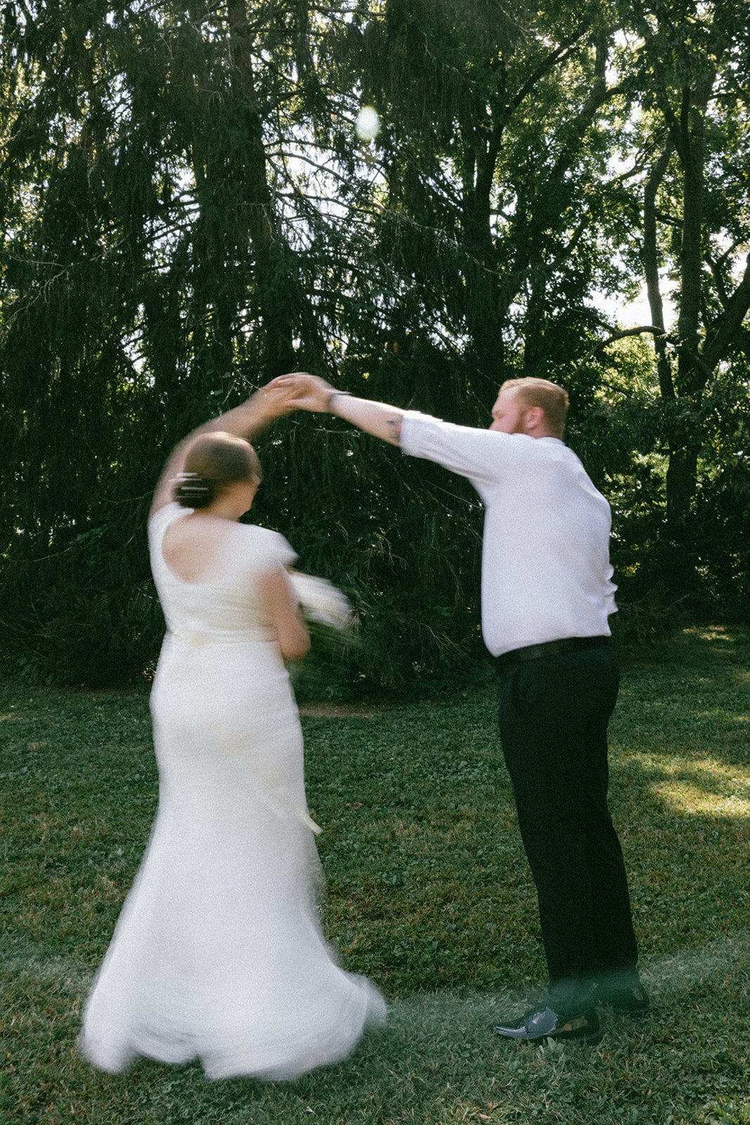 Groom twirls bride in blurry photo under summer trees in TN. 