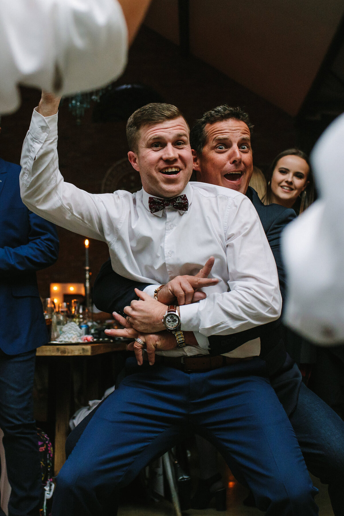 The groom and a guest are dancing while pulling a funny face on the dance floor. 