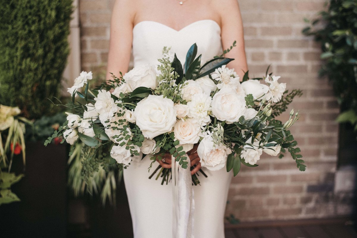 bride holding overgrown bouquet of white roses and greenery with ivory ribbon streamer