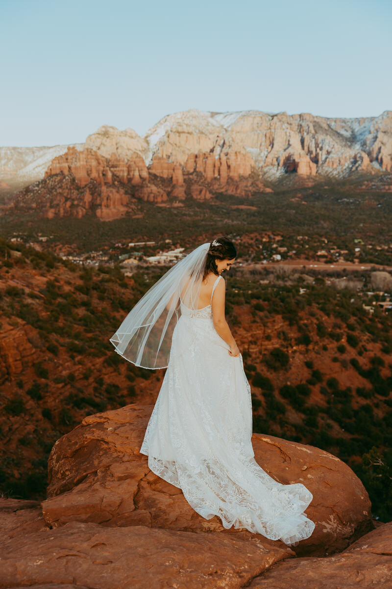 woman stands in a wedding dress on cliff edge