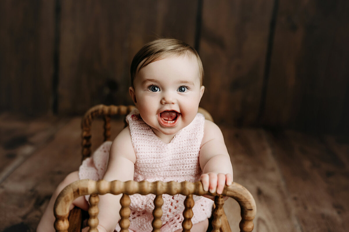 Adorable baby girl sitting in a wooden crib smiling at her Fort Collins photo shoot