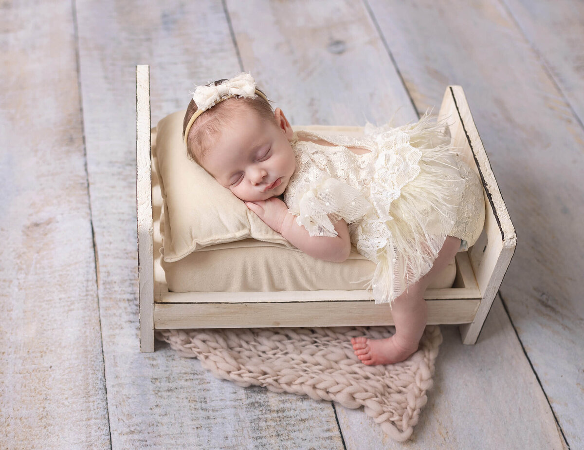 newborn baby laying on tiny bed in photoshoot