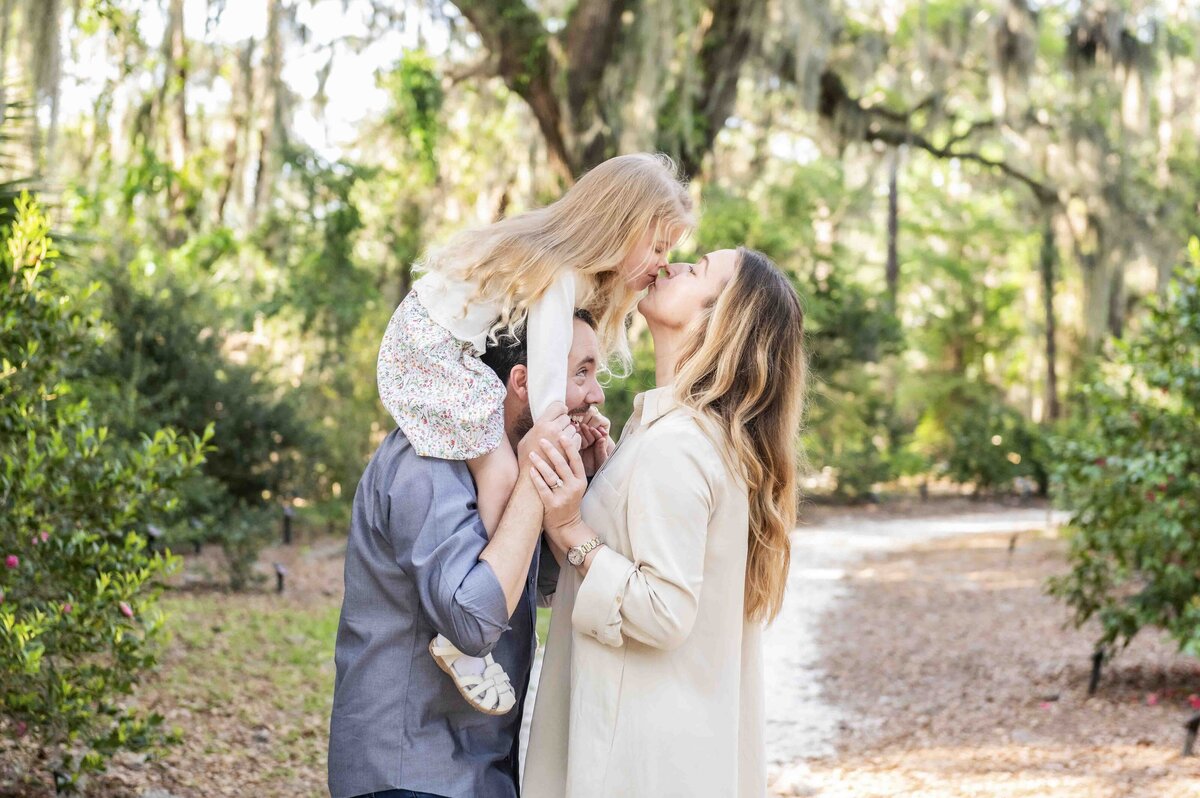 girl on dad's shoulders kissing mom in park