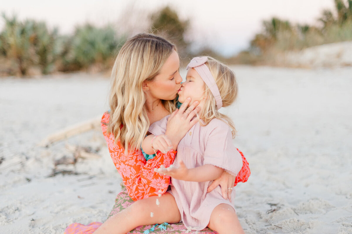 Mom kissing daughter while sitting in the sand