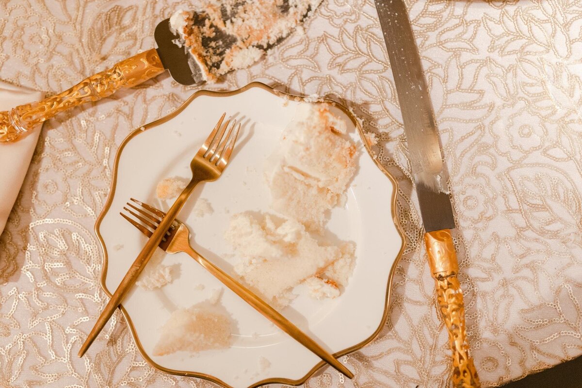 An almost empty plate with cake crumbs, two forks, and a cake server on a patterned tablecloth.