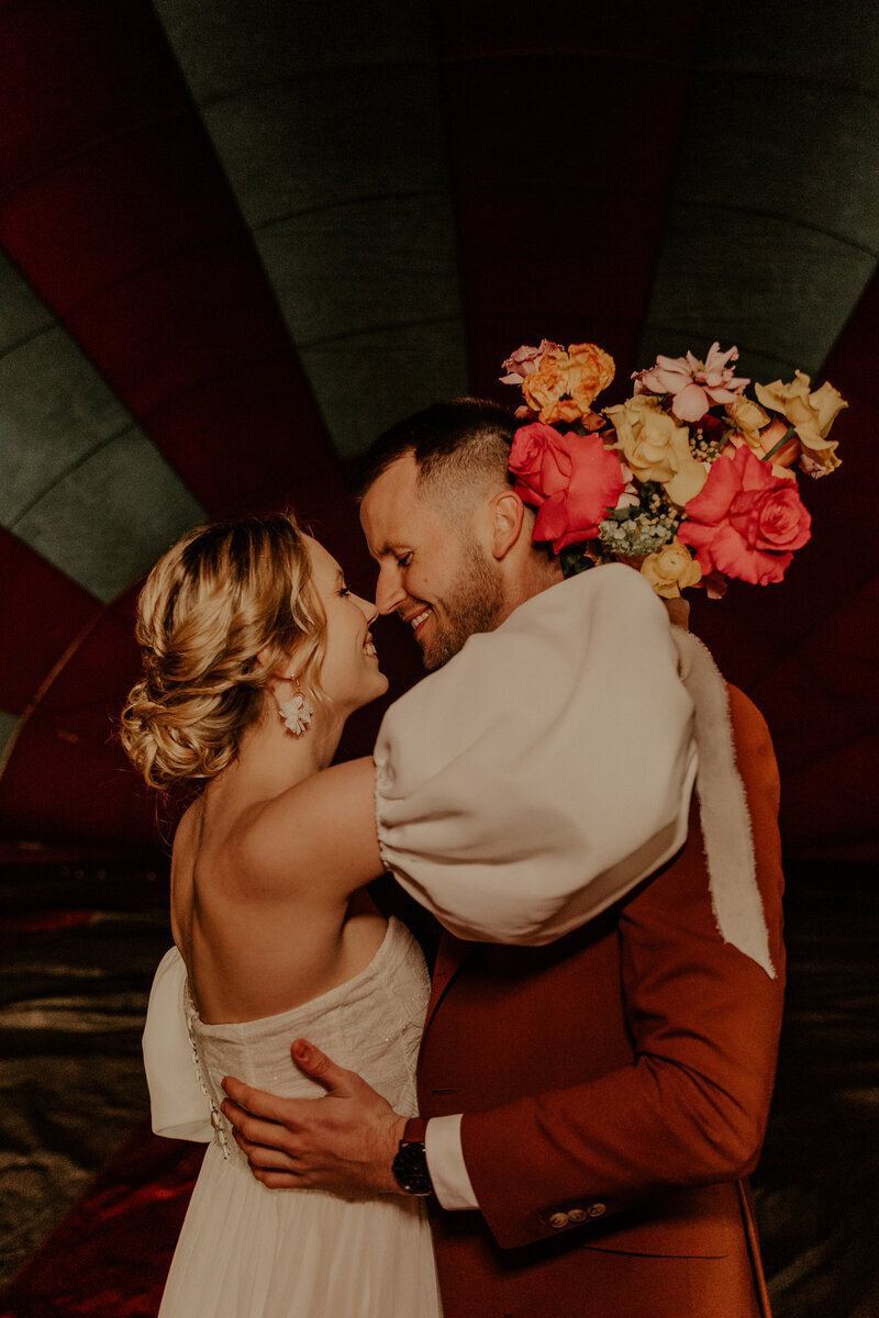 Mariés enlacés dans l'intérieur d'un ballon bariolé rouge et blanc d'une montgolfière capturés par Laura, photographe de mariage.