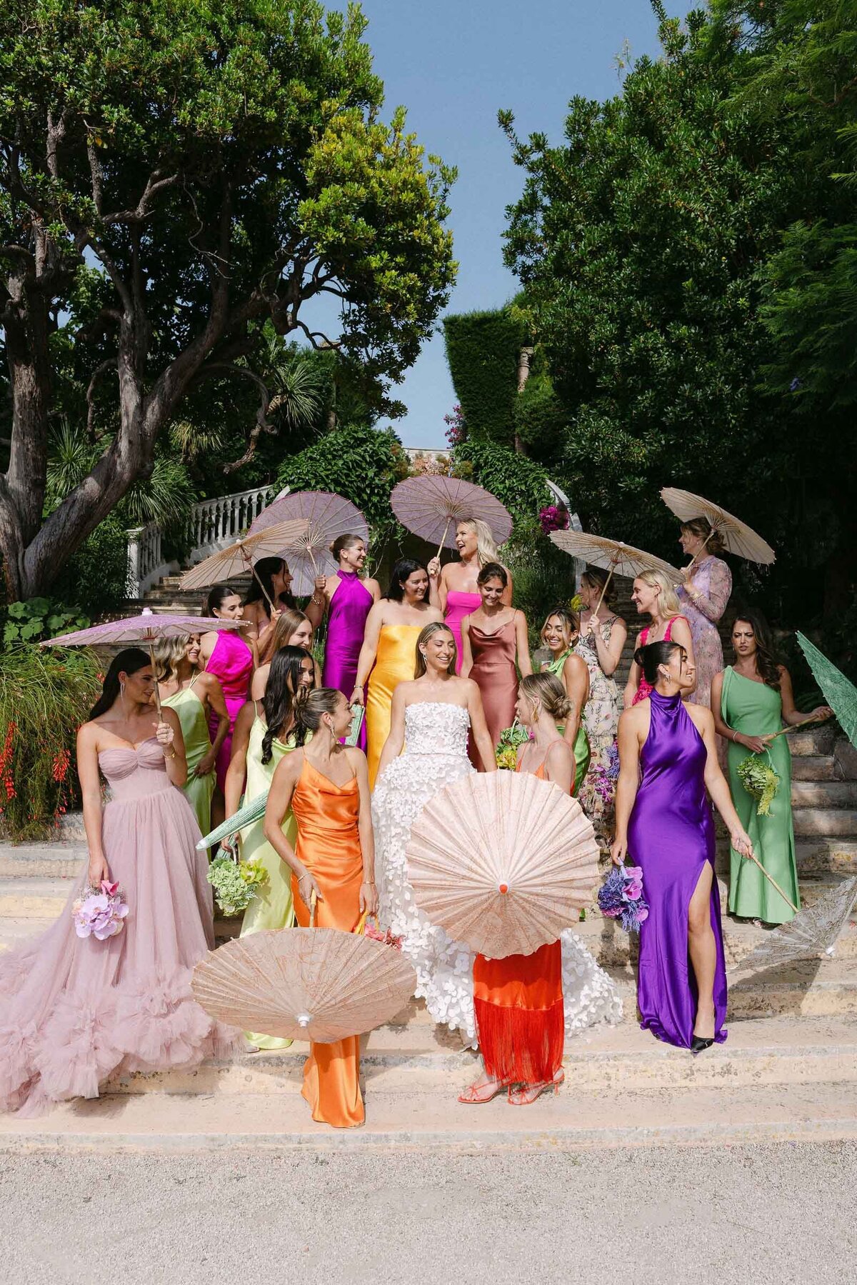 Bride with her bridesmaids holding summer umbrellas and wearing coloful fashionable dresses.